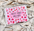 A boxed product labeled 'PRETTY THINGS GIRLS NEED' with a pink strawberry pattern, placed on a soft beige textured blanket.